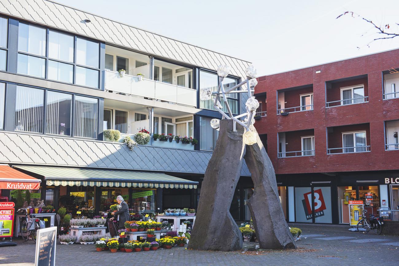 pleintje tussen duplexen met winkels en klein kunstwerk in het midden