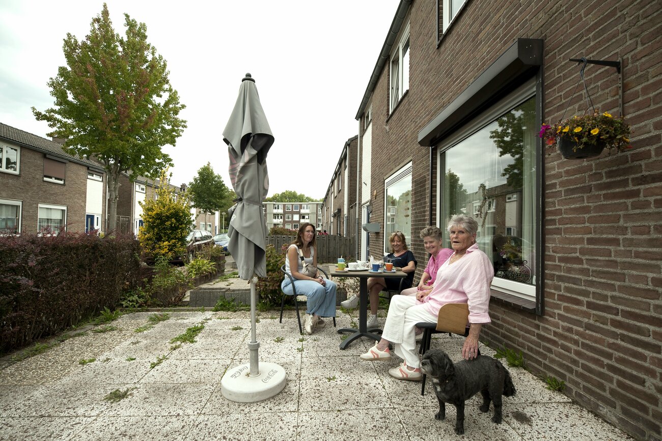 een bankje voor een huis onder een raam met mensen en een hond