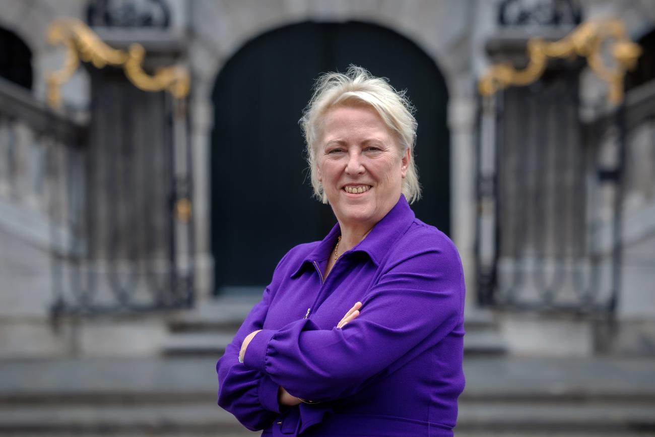 Blonde vrouw in paarse blouse staat met armen over elkaar voor het stadhuis.